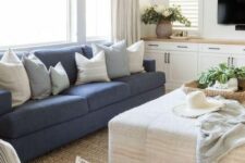 a modern farmhouse living room with built-in cabinets, a blue sofa, a neutral ottoman, neutral chairs, a jute rug and some greenery
