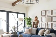 a modern farmhouse neutral living room with a blue sofa, a gallery wall, a round coffee table and mismatching chairs, a stylish chandelier
