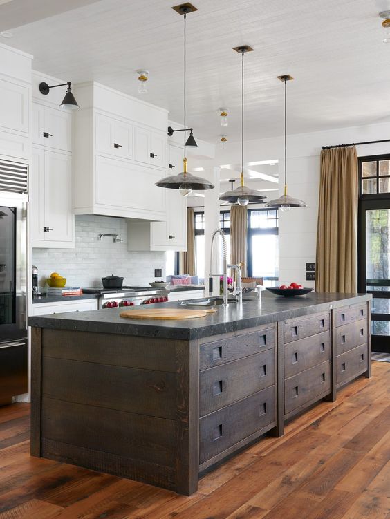 A modern kitchen with white cabinets, a white subway tile backsplash, a dark stained kitchen island and pendant lamps