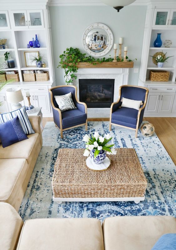 A nautical living room with a fireplace, built in storage units, a tan sectional, navy chairs and sofas