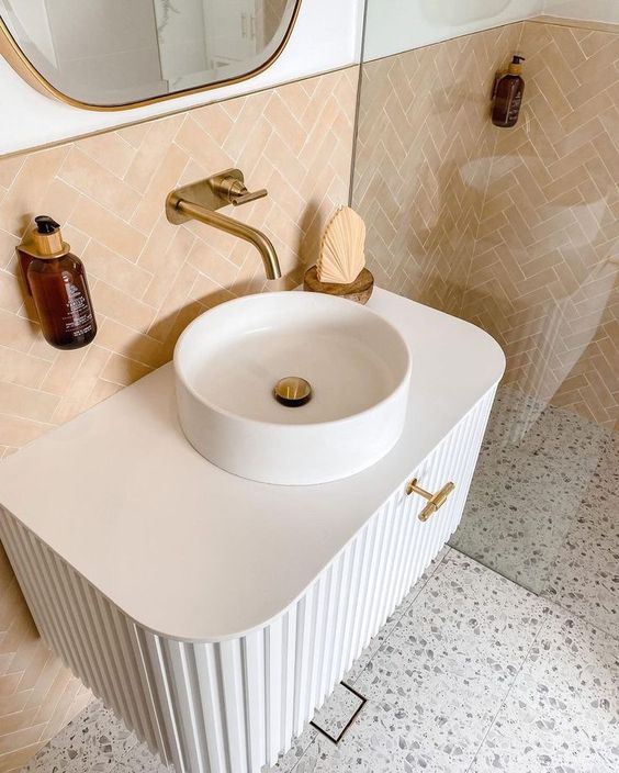 a neutral bathroom done with terrazzo, peachy tiles, a fluted white vanity with a vessel sink and a shower space
