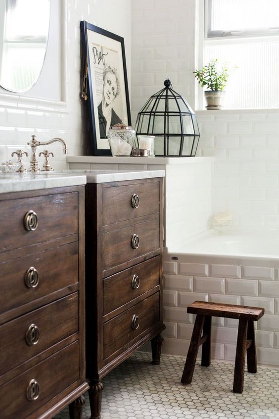 A neutral bathroom with dark stained vanities, a bathtub clad with tiles, vintage fixtures and a dark stained stool