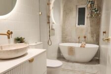 a neutral bathroom with skinny tiles and stone tiles, a white reeded vanity with a vessel sink, an oval tub and pendant planters with greenery