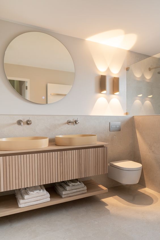 a neutral contemporary bathrooom with a shower, a fluted vanity with a shelf, vessel sinks, a round mirror and a toilet