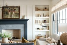 a neutral farmhouse living room with wooden beams, built-in shelves, a fireplace with a black mantel, a white sofa, a blue one, a coffee table
