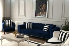 a neutral living room with a navy sofa and chair, a creamy sofa, a vintage coffee table and striped pillows and a rug plus a chic crystal chandelier