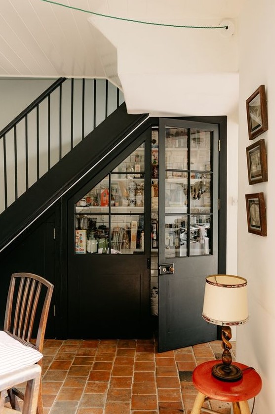 a pantry built in under the staircase, with elegant French doors and open shelves and railings inside is a perfect solution