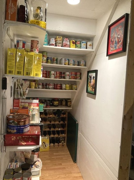 A practical staircase pantry with built in shelves and open shelving, with tain boxes and containers plus a wine bottle stand