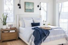 a pretty modern coastal bedroom with beadboard walls, blue bedding, a nautical artwork, wooden furniture and a jute rug