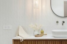 a refined contemporary bathroom with white skinny tiles, a fluted floating vanity, an oval mirror, a pendant lamp