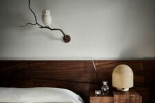 a refined contemporary bedroom clad with dark-stained wood, with a low bed, a nightstand, a table lamp and a branch with an owl as decor