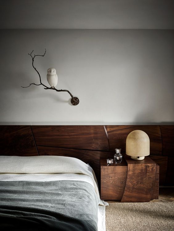 a refined contemporary bedroom clad with dark-stained wood, with a low bed, a nightstand, a table lamp and a branch with an owl as decor