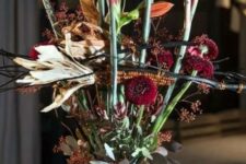 a scary Halloween floral arrangement with orange and burgundy blooms and greenery plus corn cobs