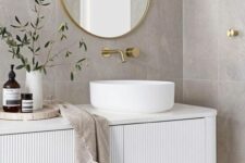 a serene bathroom with grey stone tiles, a white fluted and curved vanity with a vessel sink, an oval mirror and greenery
