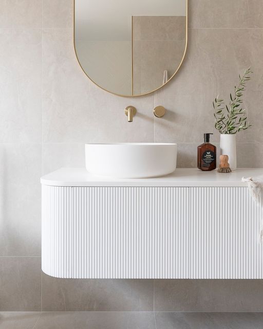 a serene neutral floating reeded vanity with a vessel sink, an oval mirror, some greenery and gold touches