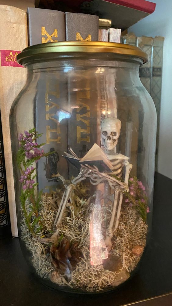 a simple Halloween terrarium with moss, a skeleton, pinecones and blooms is a catchy decor idea