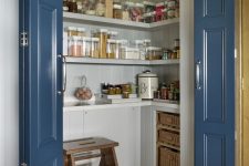 a small and chic pantry with built-in cabinets, open shelves, baskets, a wooden stool and some jars is a super cool idea