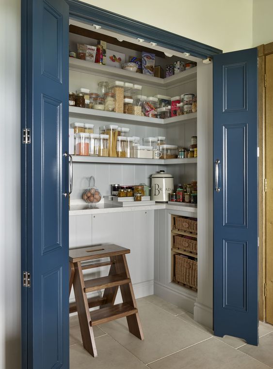 A small and chic pantry with built in cabinets, open shelves, baskets, a wooden stool and some jars is a super cool idea