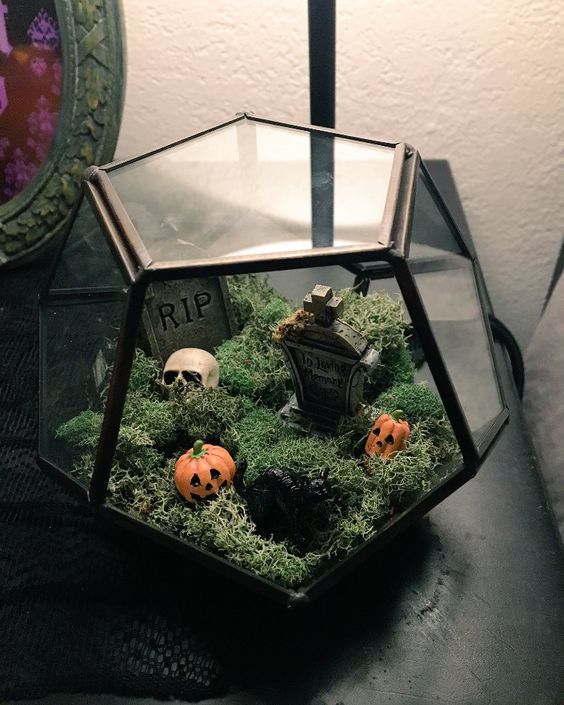 A small and pretty Halloween terrarium with moss, a graveyard and mini jack o lanterns is a lovely decor idea