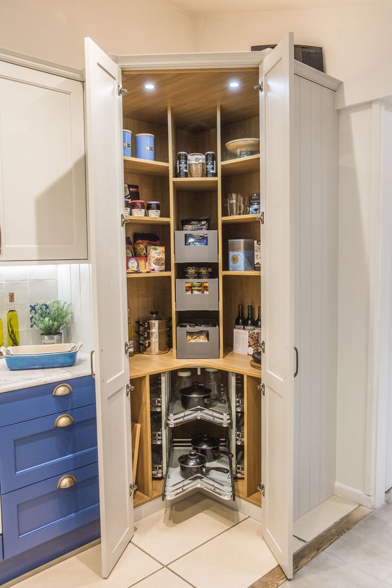 A small corner pantry with open shelves, drawers, built in lights, cookware and food, some wine bottles