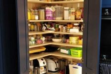a small pantry built in the kitchen, with navy doors, corner open shelves, cubbies and lots of jars and containers plus built-in lights