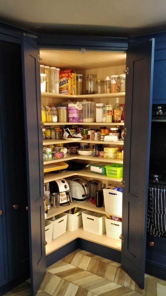 A small pantry built in the kitchen, with navy doors, corner open shelves, cubbies and lots of jars and containers plus built in lights