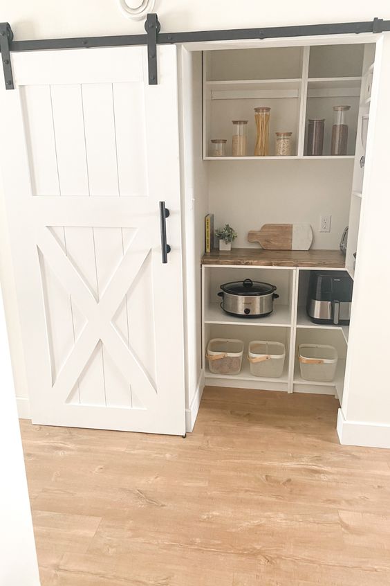a small pantry with a barn door, open storage units, cookware and cubbies is a cool solution for a rustic space
