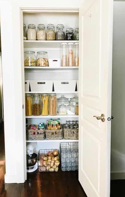 a small pantry with open shelves, cubbies, wire baskets, jars and containers and a door that hides it all away