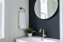 a small powder room with a soot accent wall, a timber vanity with a stone sink, a round mirror and pendant lamps