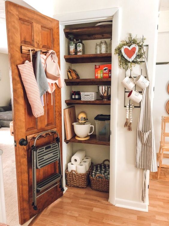 a small rustic pantry with stained shelves, baskets and jars for storage and some stuff, a stool and some things
