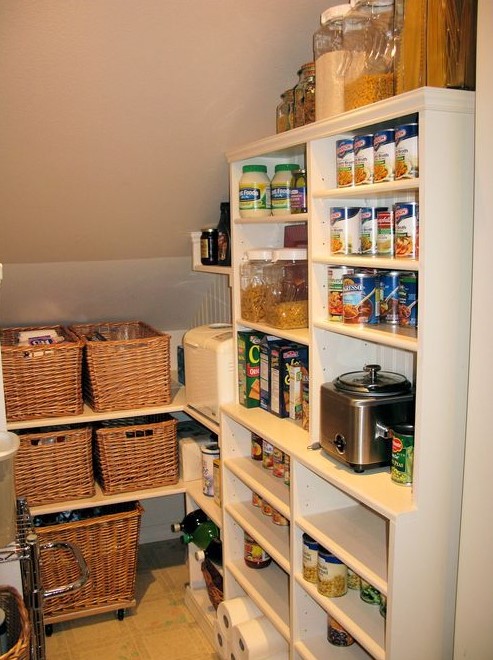 a small staircase pantry with built-in shelves and a large open storage unit, baskets and plastic and glass containers