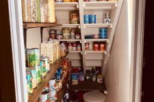 a small under stairs pantry with open shelves on the wall and built right into the staircase, with lights for more comfrotable using