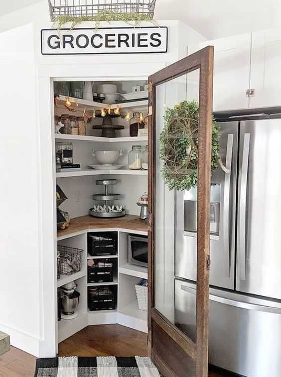 A small well organized pantry with corner shelves and built in open storage units, with lights and some tableware