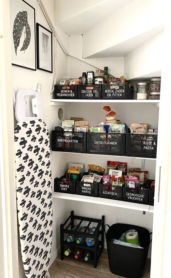 a small yet cool under stairs pantry with open shelves, black cubbies, black boxes for storage and some art and lights