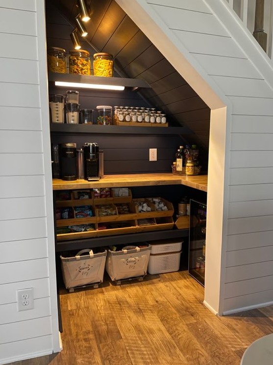 A small yet stylish farmhouse pantry with black shiplap inside, built in shelves and a countertop, cubbies and a wooden shelf