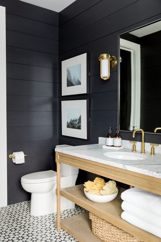 A soot bathroom with a light stained vanity abd baskets, a mirror, sconces and a mini gallery wall is cool