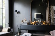 a soot living room with a black console and a chic mirror, blush chairs, a grey sofa, eye-catching coffee tables