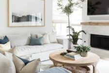 a soothing living room with a built-in fireplace, neutral sofas, blue and white pillows, a wooden coffee table and greenery