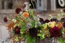 a sophisticated Halloween flower arrangement of orange, burgundy and deep purple blooms, some greenery, herbs and twigs