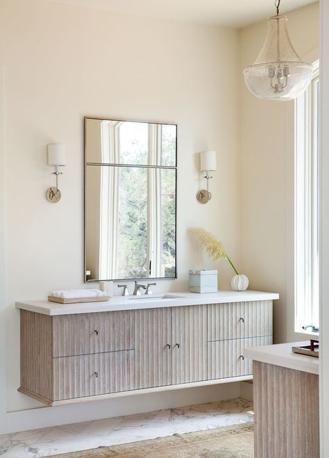 a stained fluted vanity with a white countertop, a mirror and elegant sconces plus a modern version of a classic chandelier