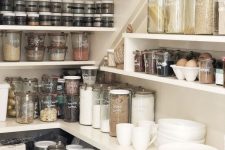 a staircase food pantry with built-in shelves, plastic and glass containers with food for a neat and elegant look and porcelain