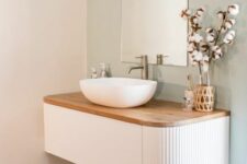 a stylish and trendy bathroom nook with an arched mirror, a white curved fluted vanity with a wooden countertop, a bowl sink