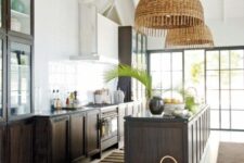a stylish kitchen with dark-stained cabinets and a large kitchen island, woven pendant lamps and greenery is amazing