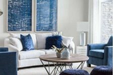 a stylish modern living room with a white sofa and blue pillows, blue chairs, midnight blue poufs, blue artwork and a coffee table