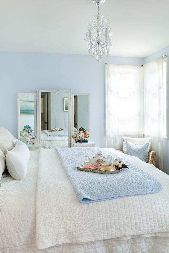 a subtle bedroom with light blue walls, a mirror, a bed with blue and white bedding, a crystal chandelier