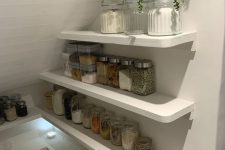 a tiny stairs pantry with open shelves with lights, a potted plant, plastic containers and glass jars with food