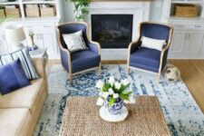 a traditional coastal living room with a tan and navy color scheme, rattan, leather and a mantel with greenery