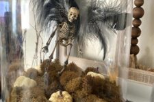 a unique Halloween cloche with moss, white pumpkins, a skeleton with black feather wings is a gorgeous idea