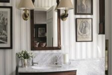 a vintage bathroom done with striped wallpaper, a dark-stained vanity, a gallerywall and a mirror in a stained frame, a couple of vintage sconces
