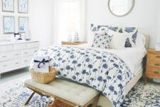 a white bedroom spruced up with blue and white textiles, with a blue and white gallery wall, a white dresser, a bed with printed bedding and a rug